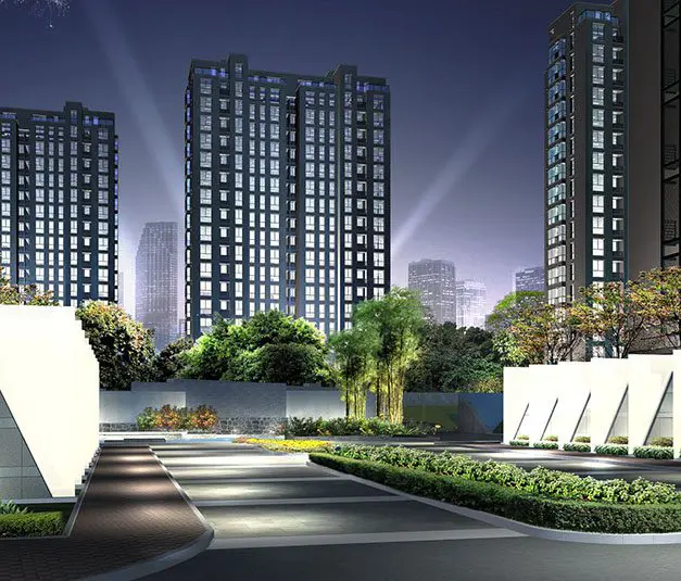 Night view of modern high-rise apartment buildings with illuminated windows, landscaped greenery, and spotlights shining in the background.