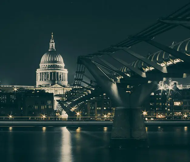 St. Paul’s Cathedral and Millennium Bridge in London at night, with illuminated buildings and reflections on the river.